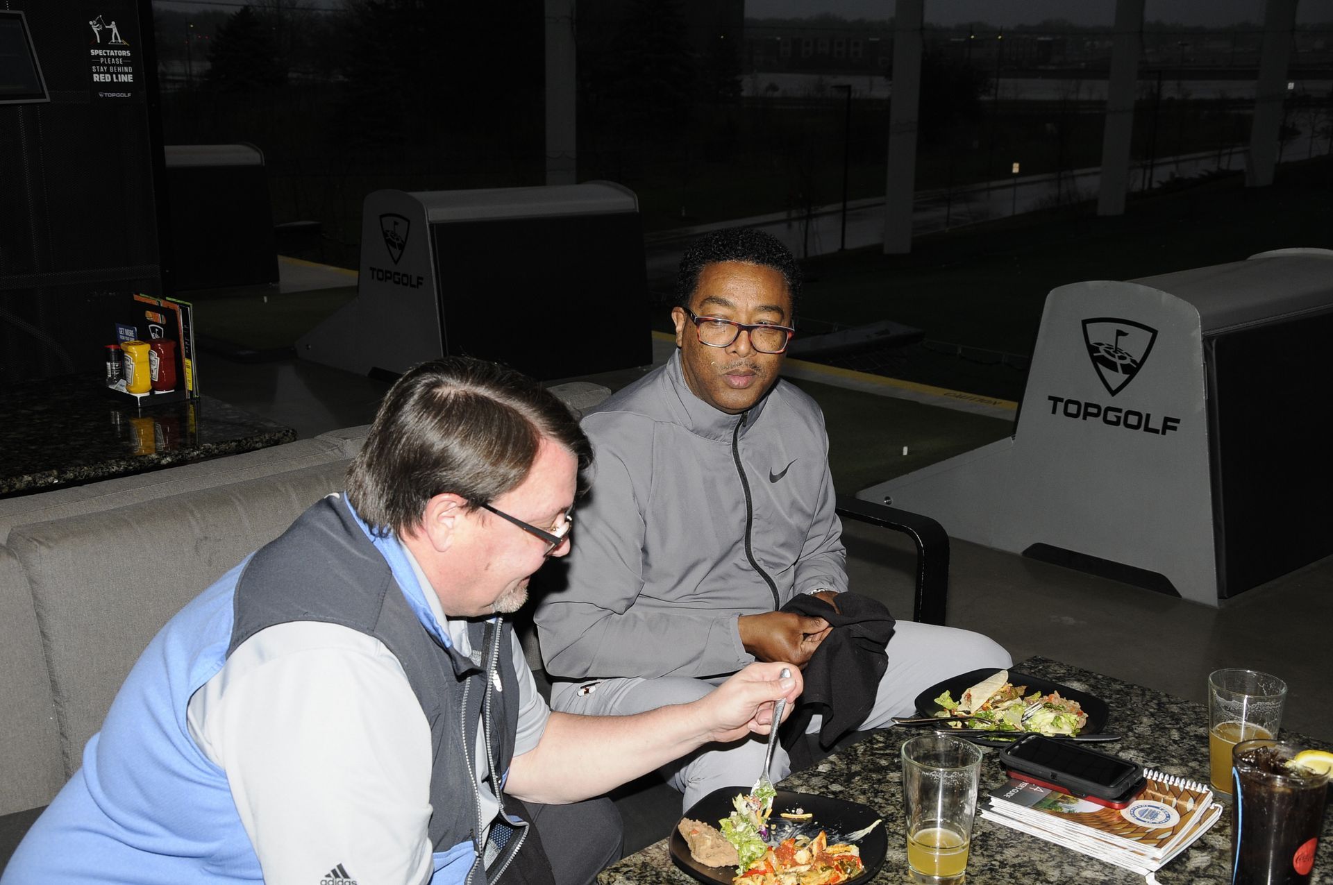 Two men are sitting at a table with food and drinks.