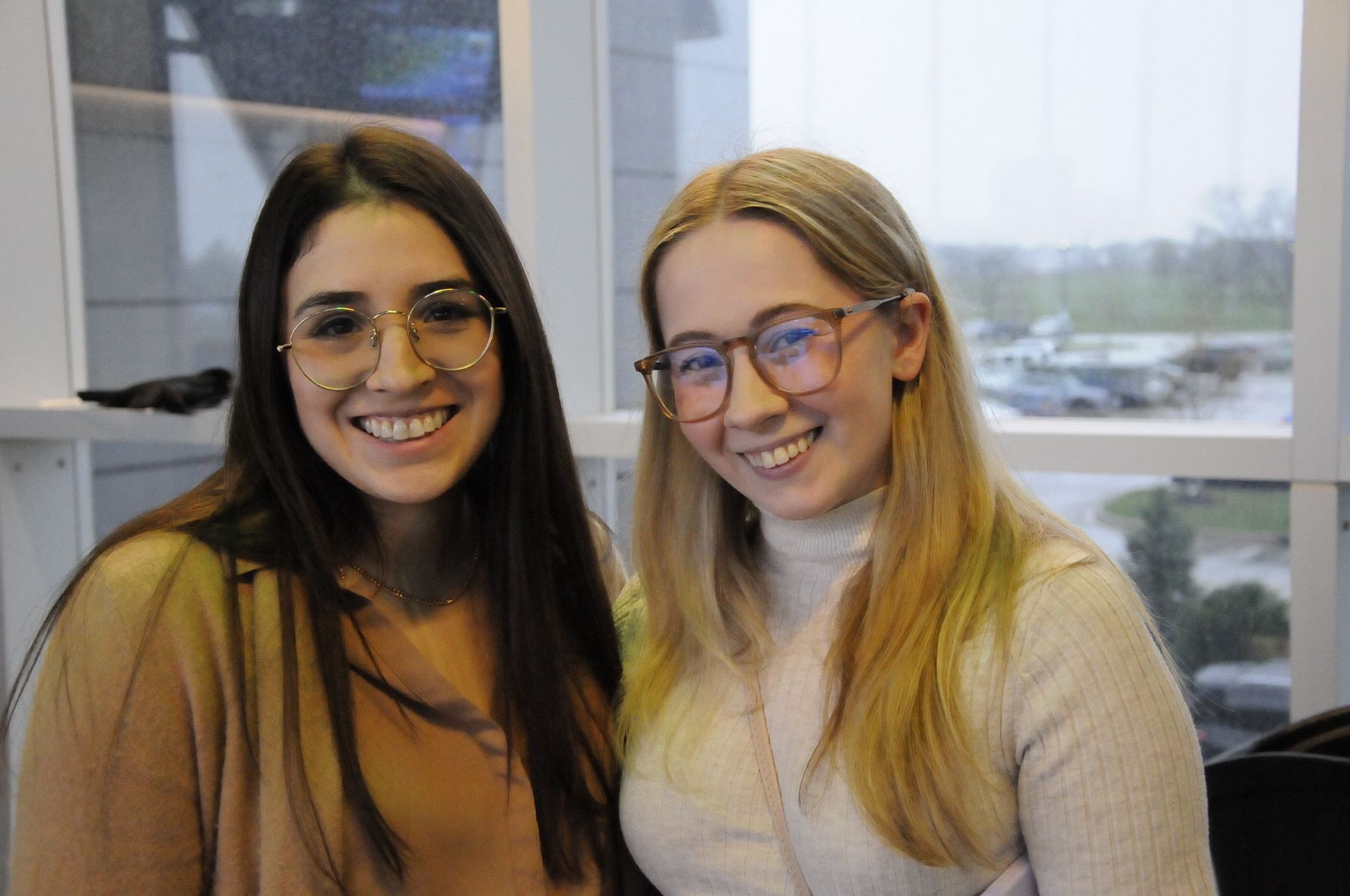 Two women wearing glasses are posing for a picture in front of a window.