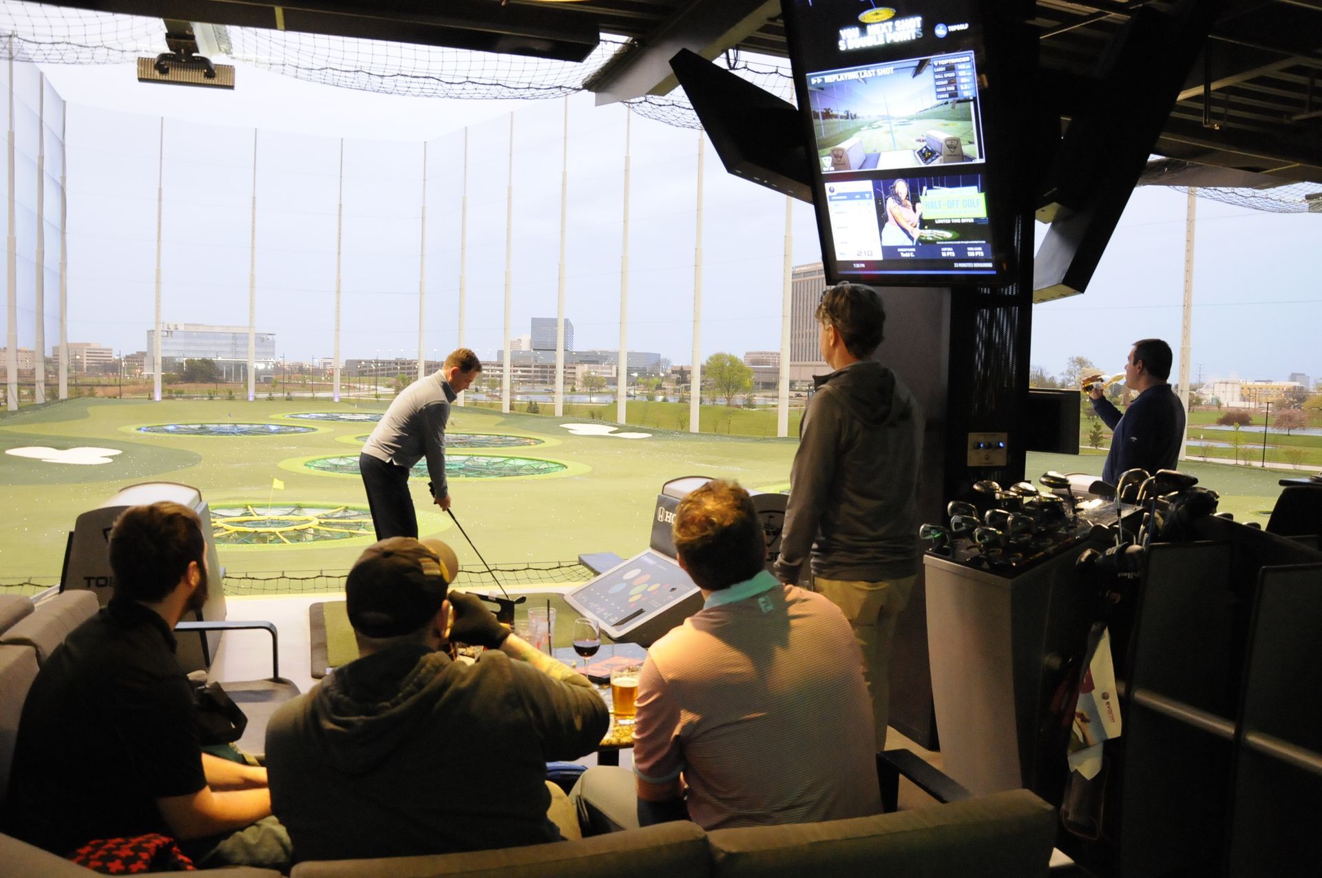 A group of people are sitting in a room watching a man play golf.