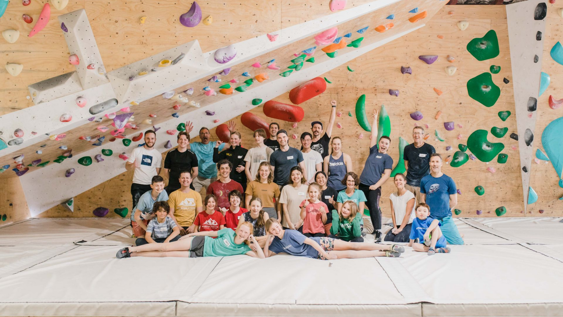 Group photo in climbing gym; people smiling in front of climbing walls with colorful holds.