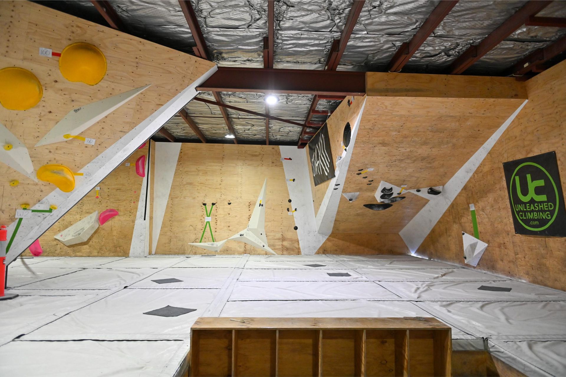 Indoor rock climbing gym with angled wooden walls, various colored holds, and safety mats.