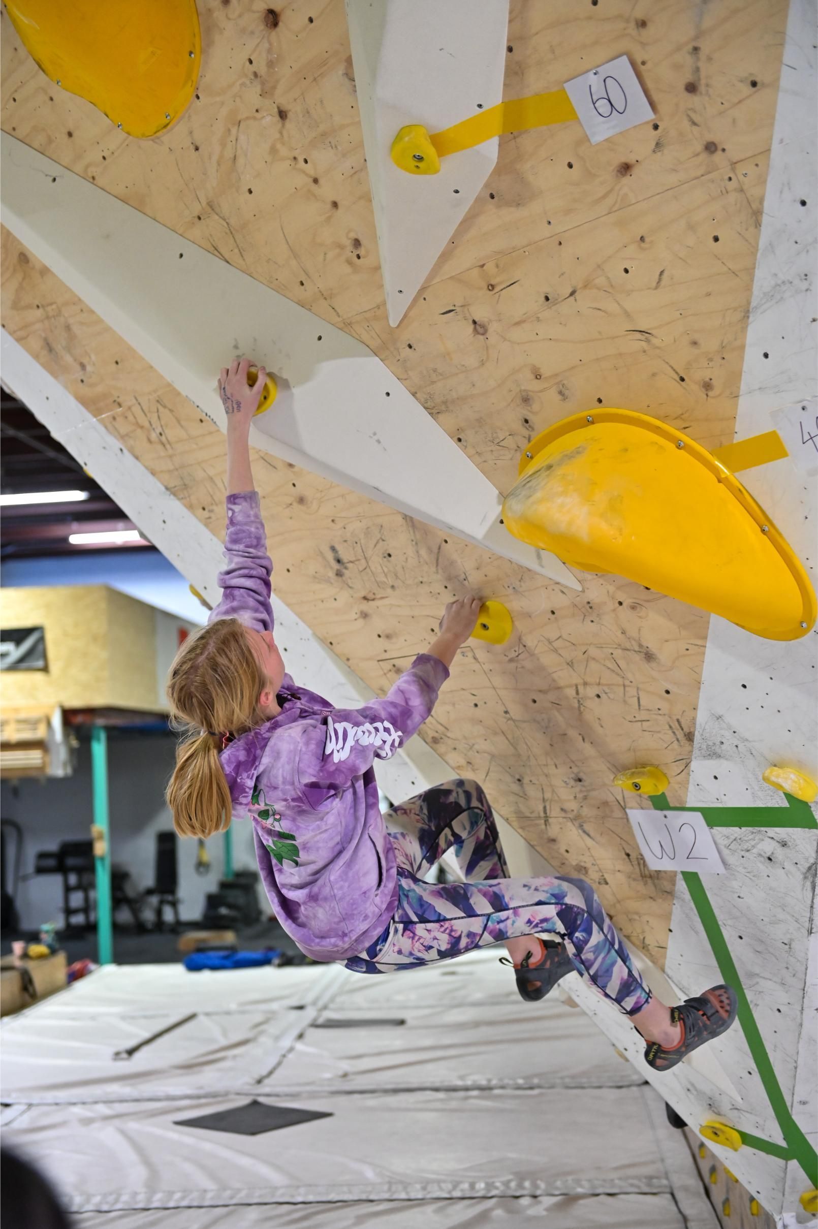 A person climbing an angled wall in a climbing gym, reaching for yellow holds.