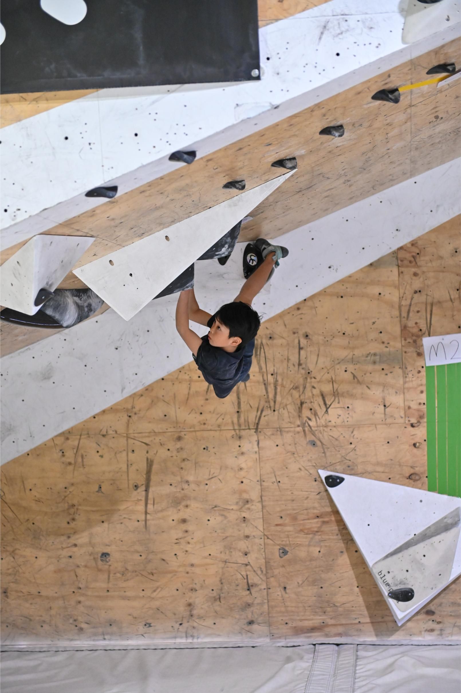Person climbing a textured indoor rock wall, reaching upward.