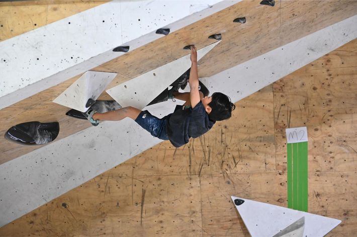 A person climbing an angled wall in a climbing gym, reaching for a handhold.