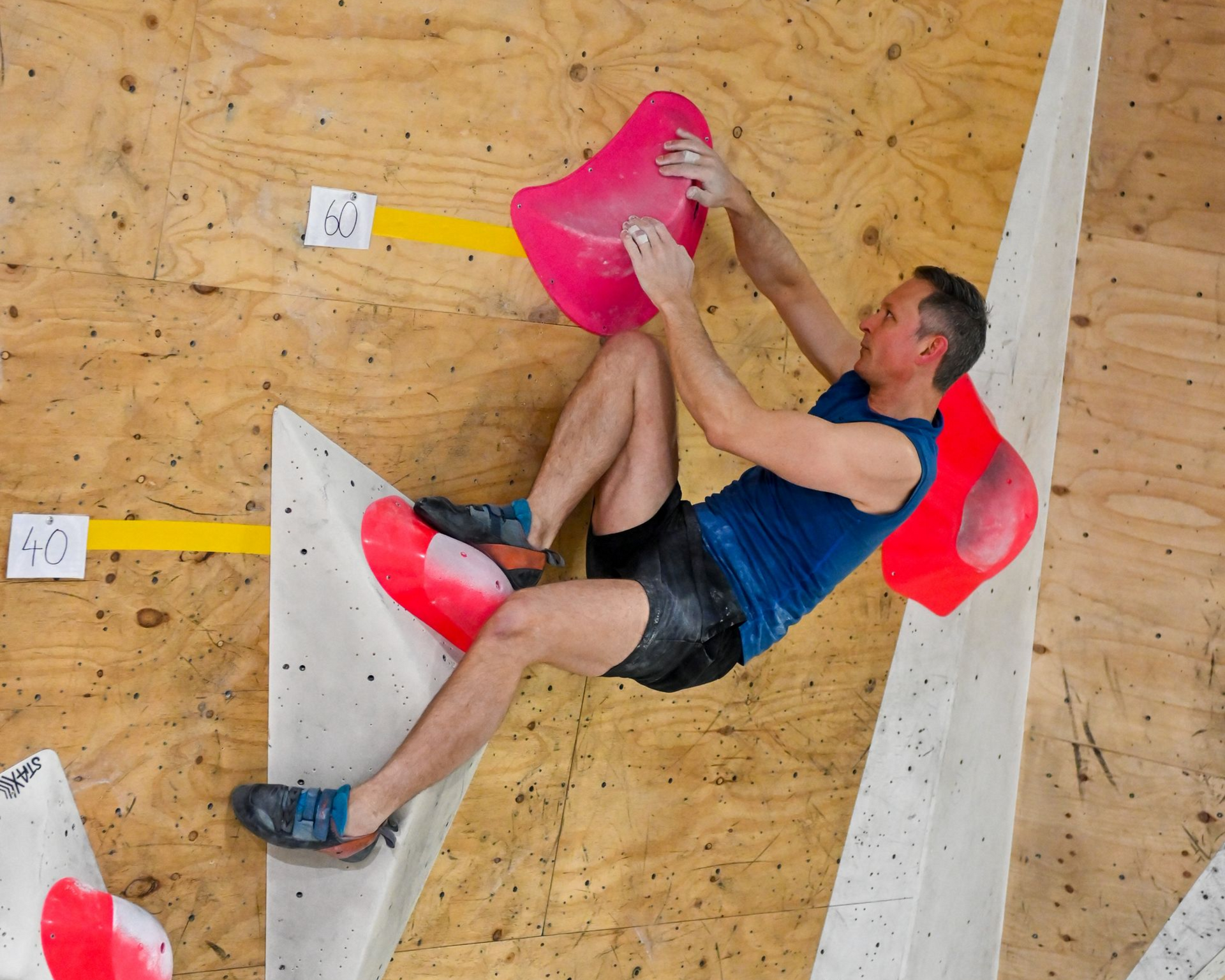 Rock climber on a wooden wall, reaching for a pink hold.