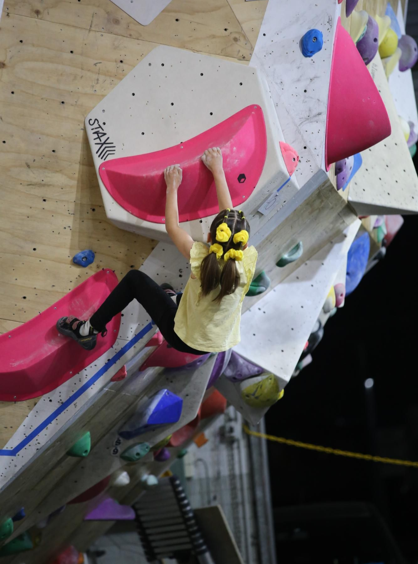 Young person climbing a colorful indoor rock wall, reaching for a pink hold.