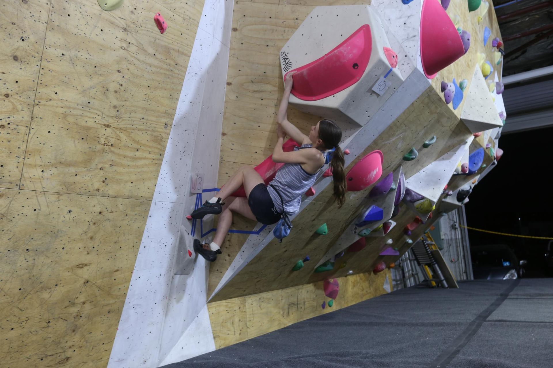 Woman climbing a steep indoor climbing wall with colorful holds.