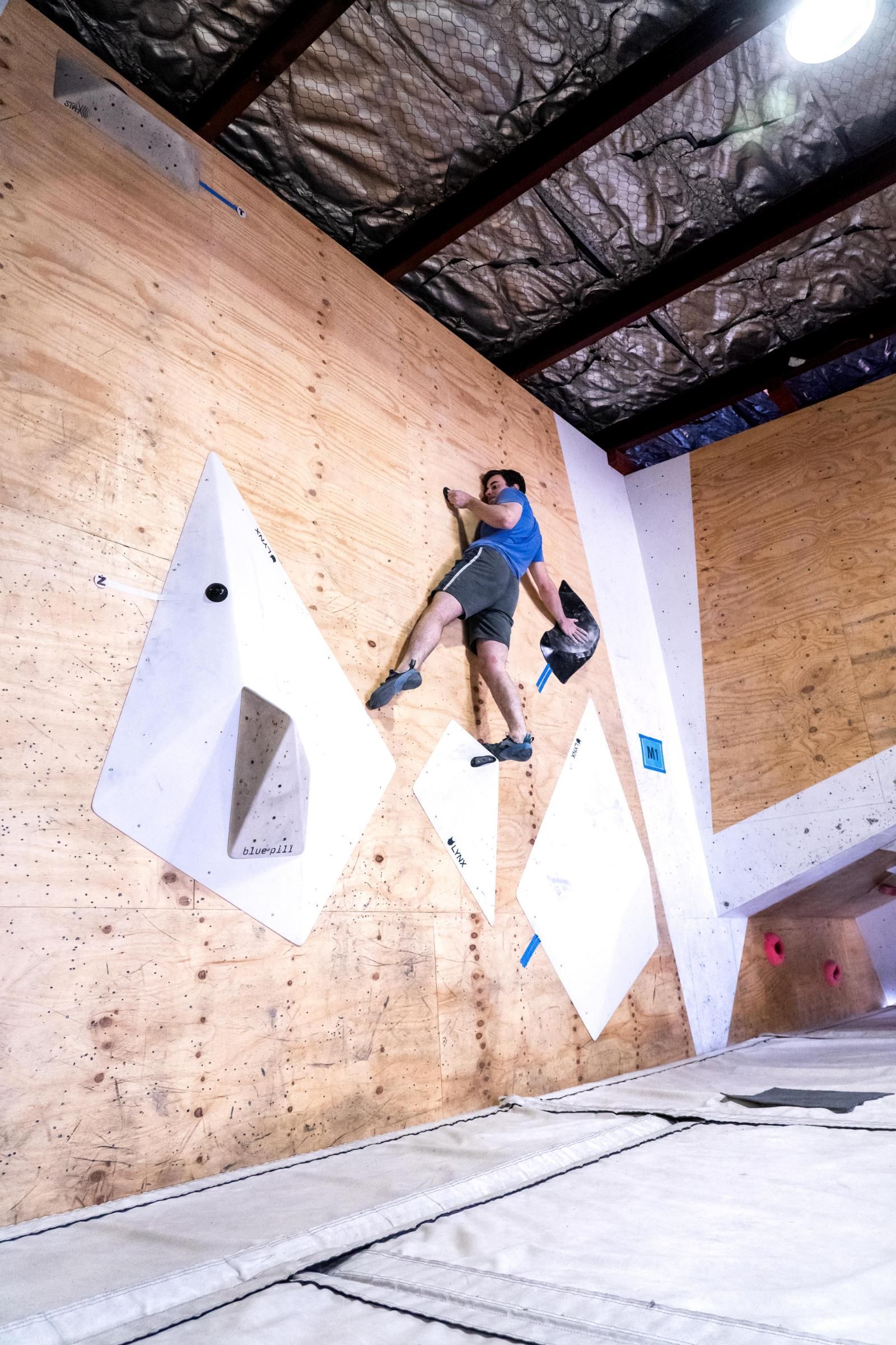 Rock climber on an indoor climbing wall with geometric holds.