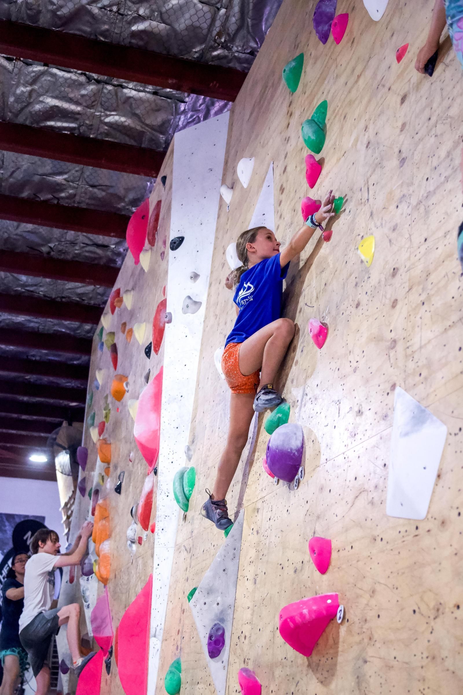 Young person climbs a brightly colored indoor rock climbing wall.