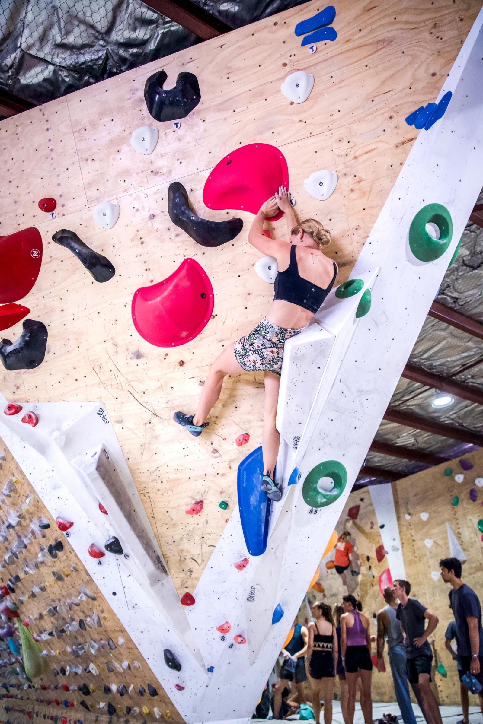 Person climbing a colorful indoor rock wall, reaching for a hold.