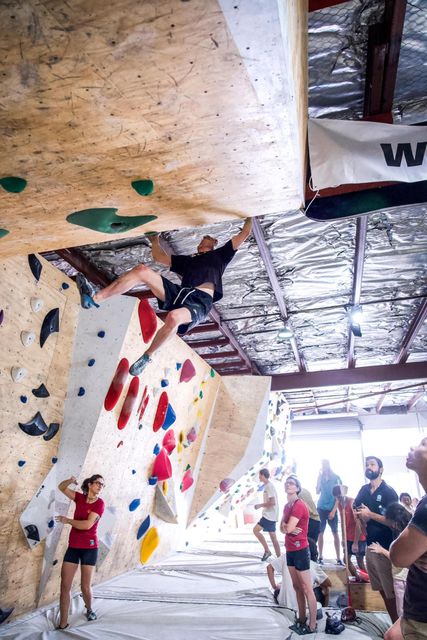 A person climbs a wall in a climbing gym. Others watch below.