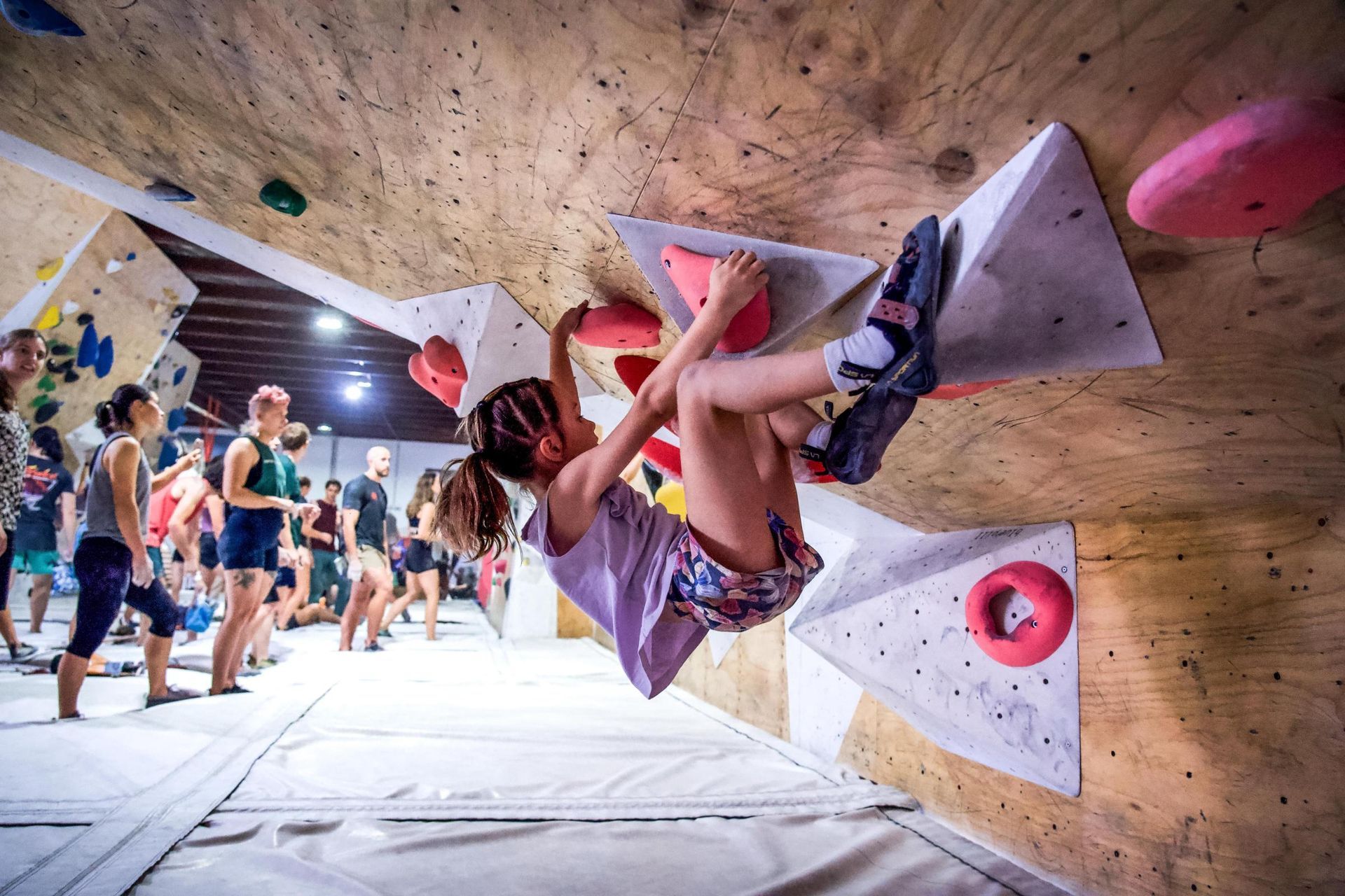 Young person climbing an indoor rock wall, reaching for holds.