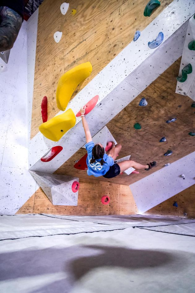 Person climbing a brightly colored indoor bouldering wall, reaching for a yellow hold.