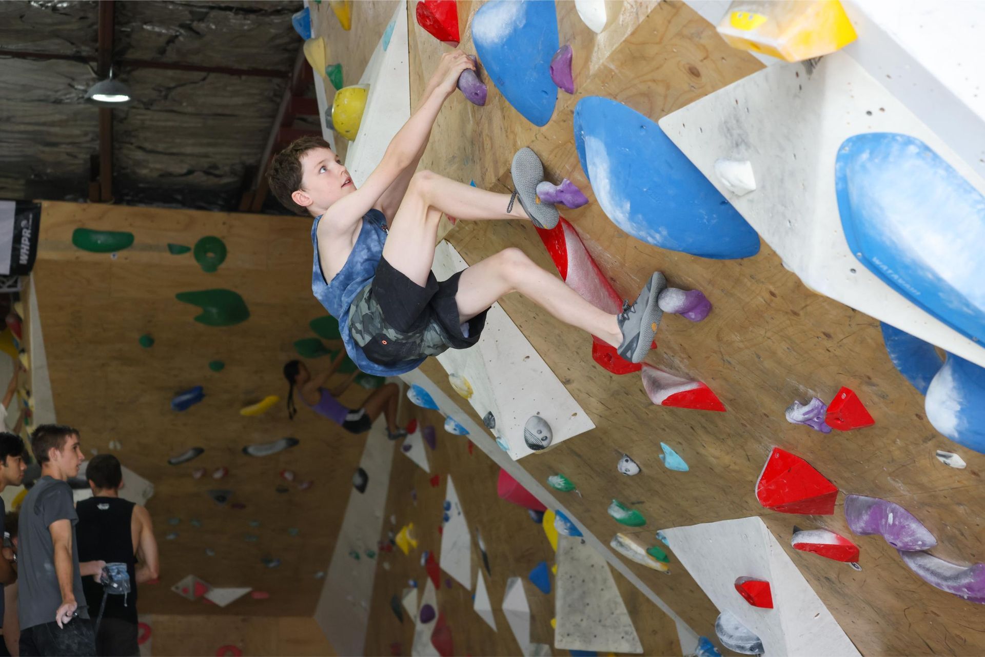 Young person climbing on an indoor rock wall, reaching for holds.
