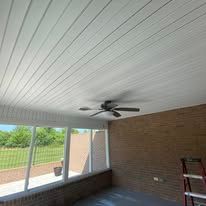 White paneled ceiling with a ceiling fan, beside a brick wall and window.
