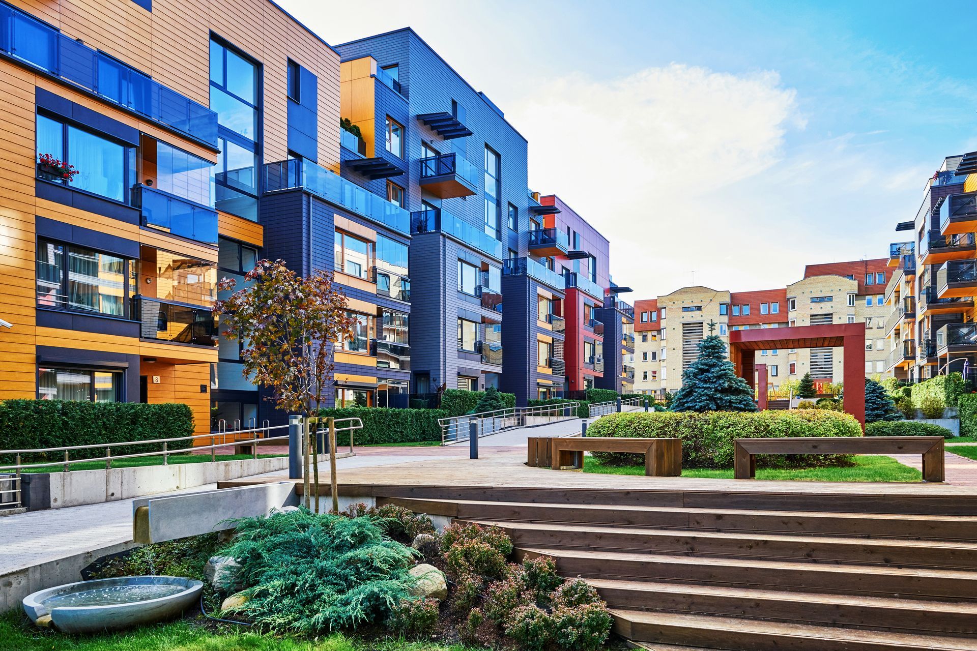 Colorful modern apartment buildings with landscaping and benches on a sunny day.