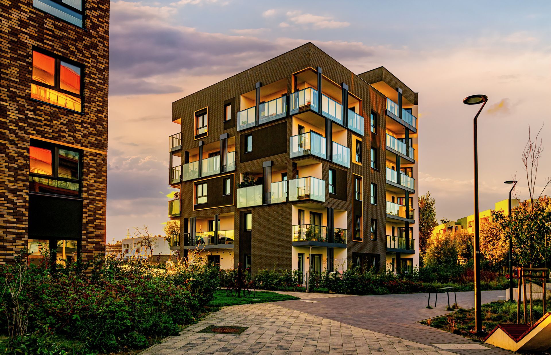 Modern apartment building with balconies, brick facade, and warm sunset lighting.
