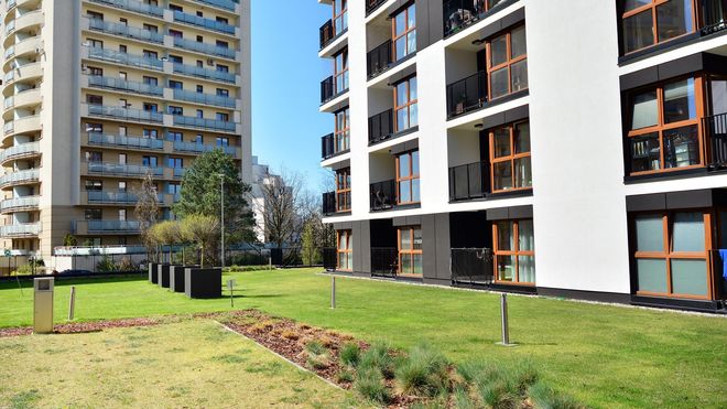 Buildings with white and beige facades, balconies, and a green lawn in between.