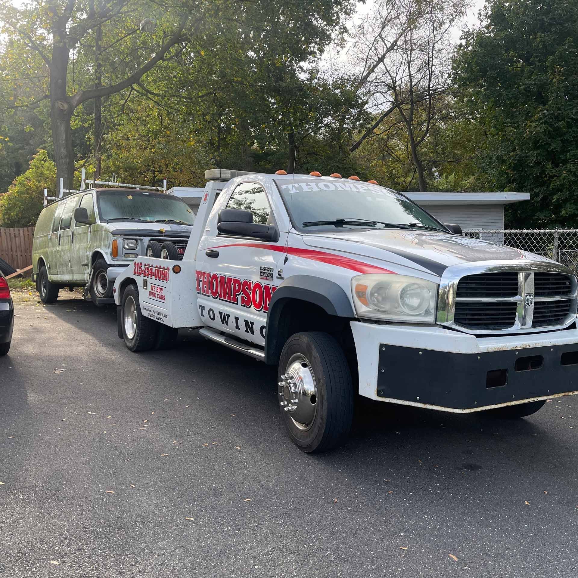 White tow truck towing a van in a parking lot. 