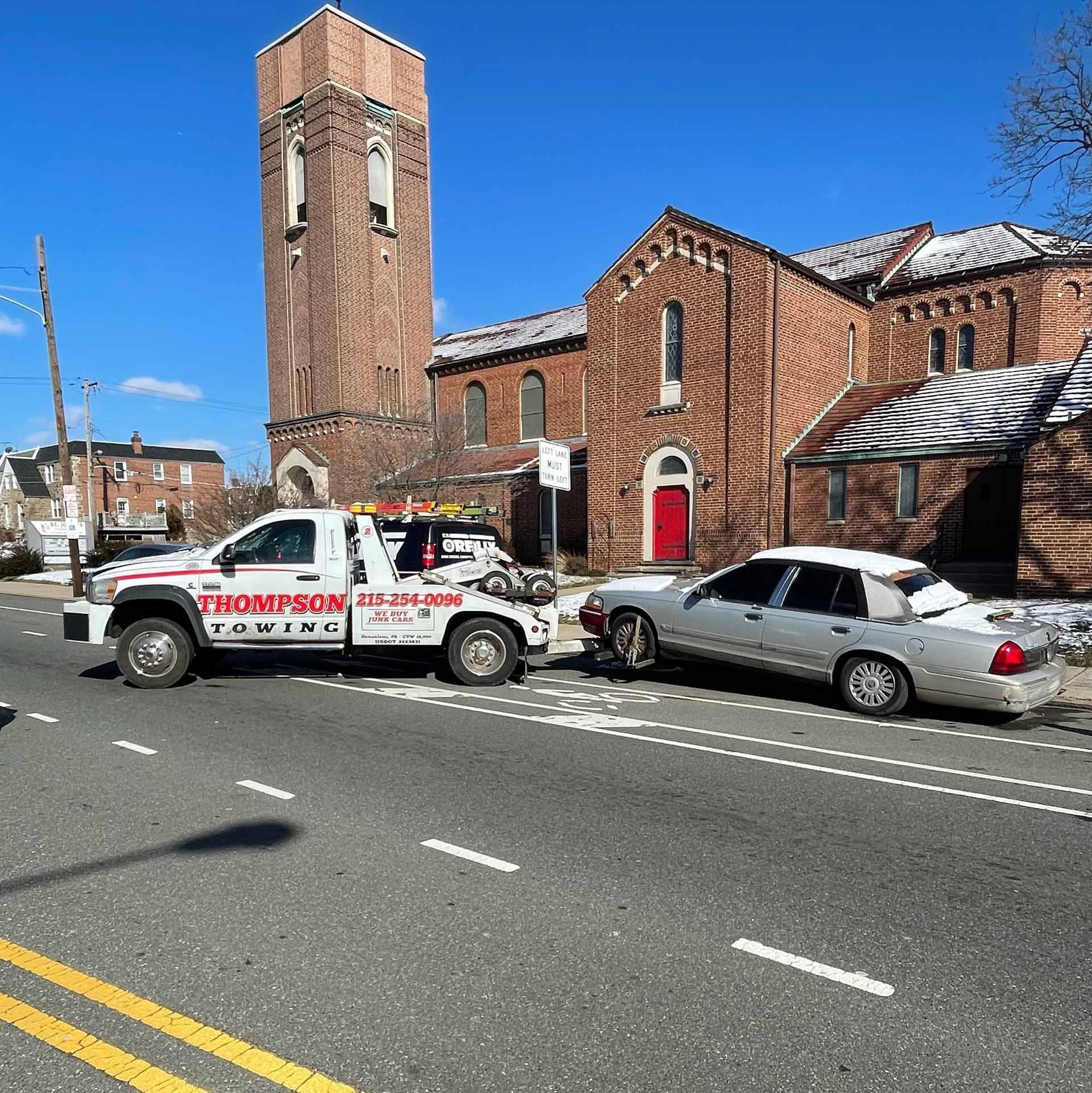A tow truck is towing a car in front of a church.