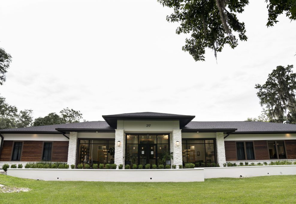A large white house with a black roof is sitting on top of a lush green field.