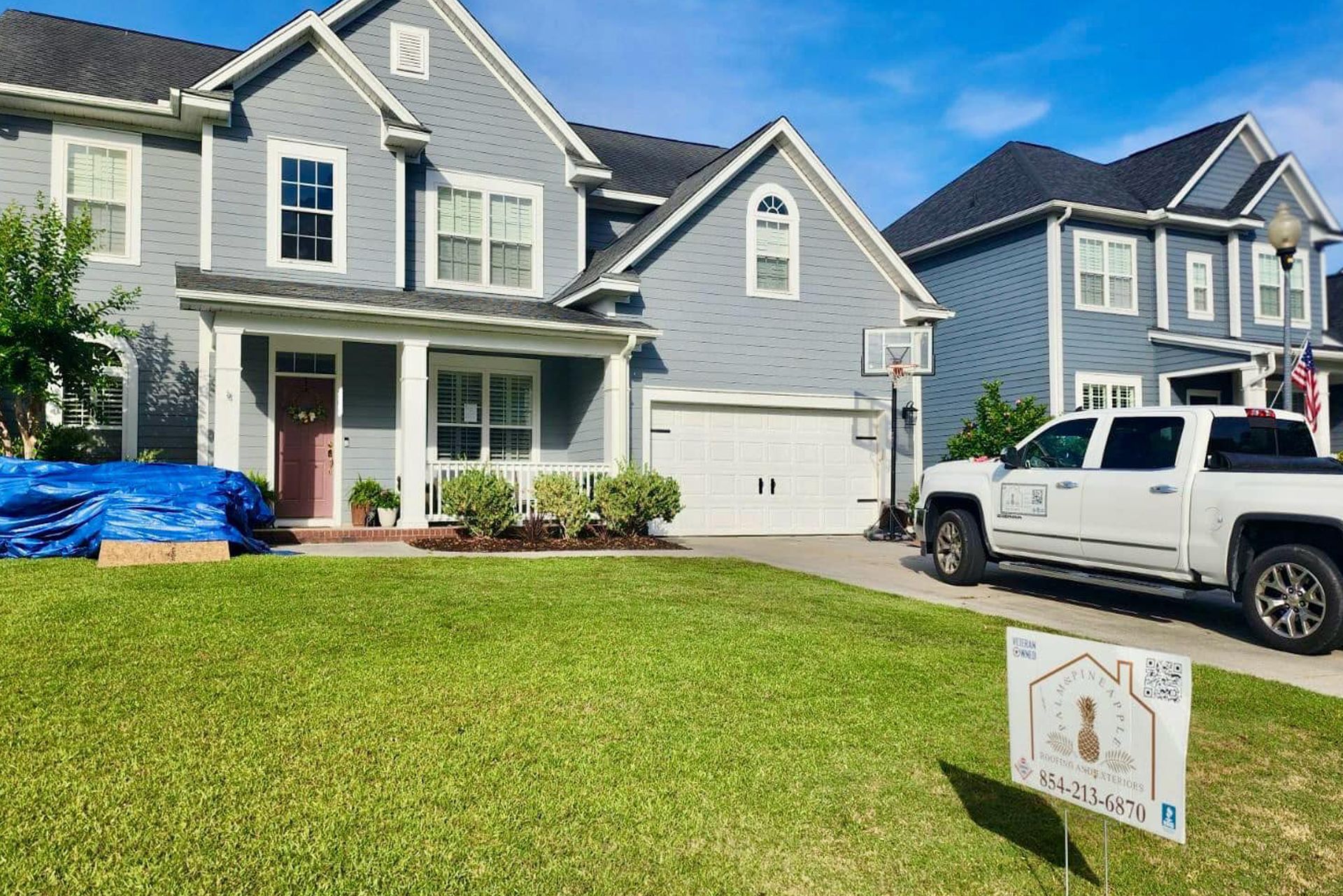 A white truck is parked in front of a gray house.