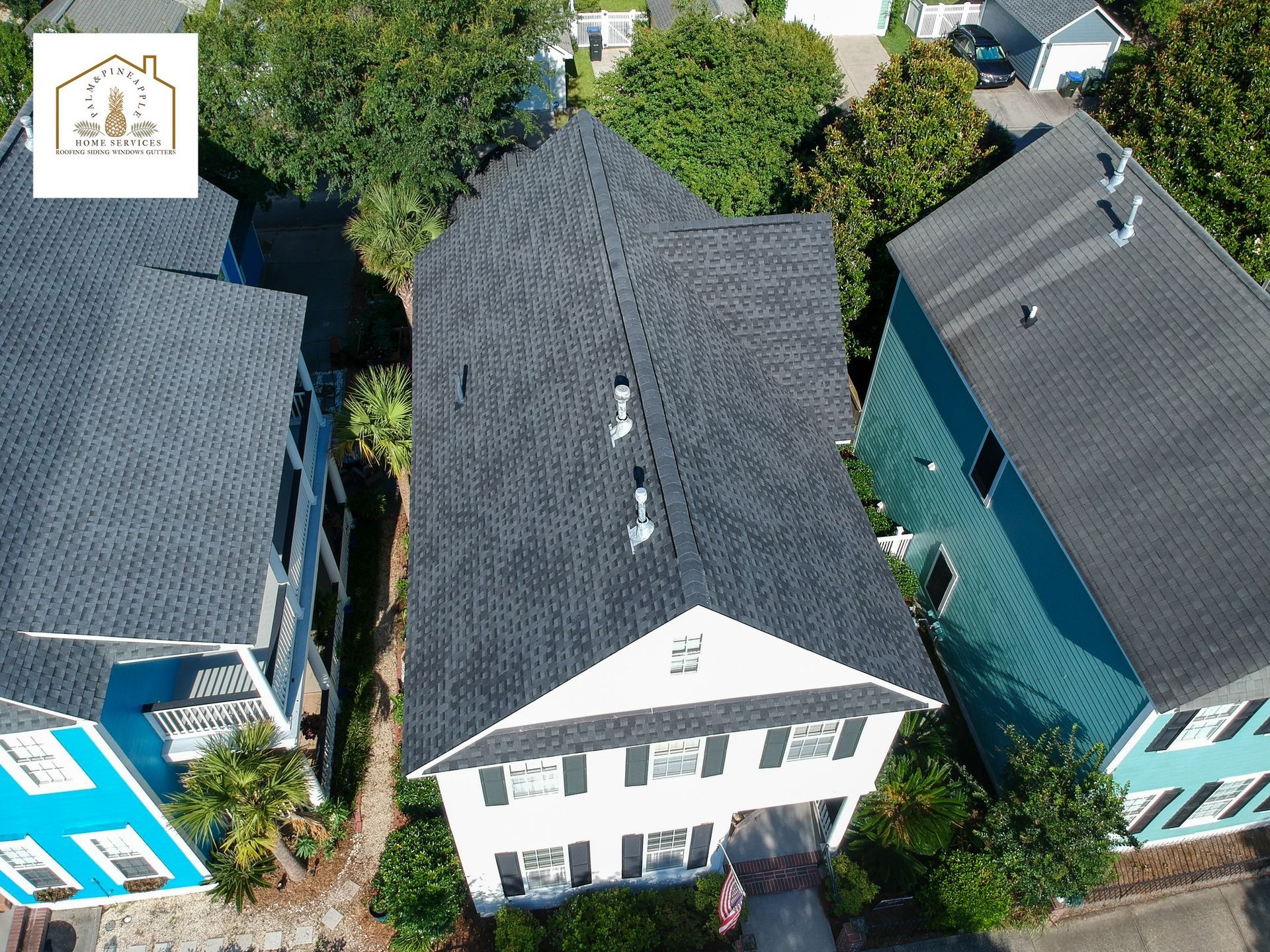 Aerial view of a white house with a dark gray roof between two colorful houses.