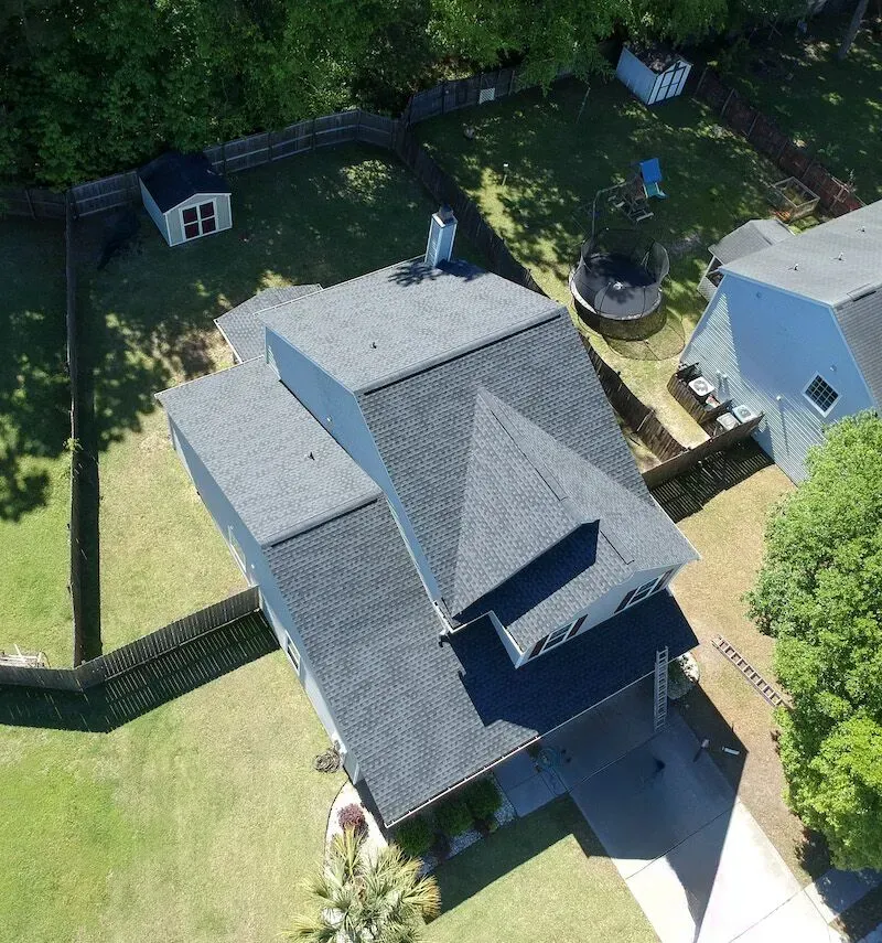 Overhead view of a house with dark gray roof, surrounded by lawn, fences, and trees.
