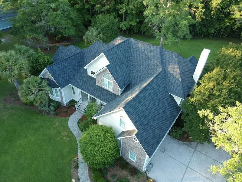 An Aerial View  House With A Blue Roof Surrounded By Trees — Summerville, SC — Palm & Pineapple Roofing and Exteriors
