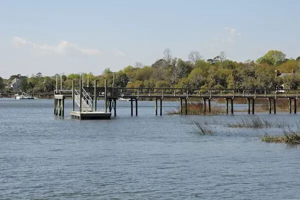 Wooden pier extending over calm blue water, trees in the background.