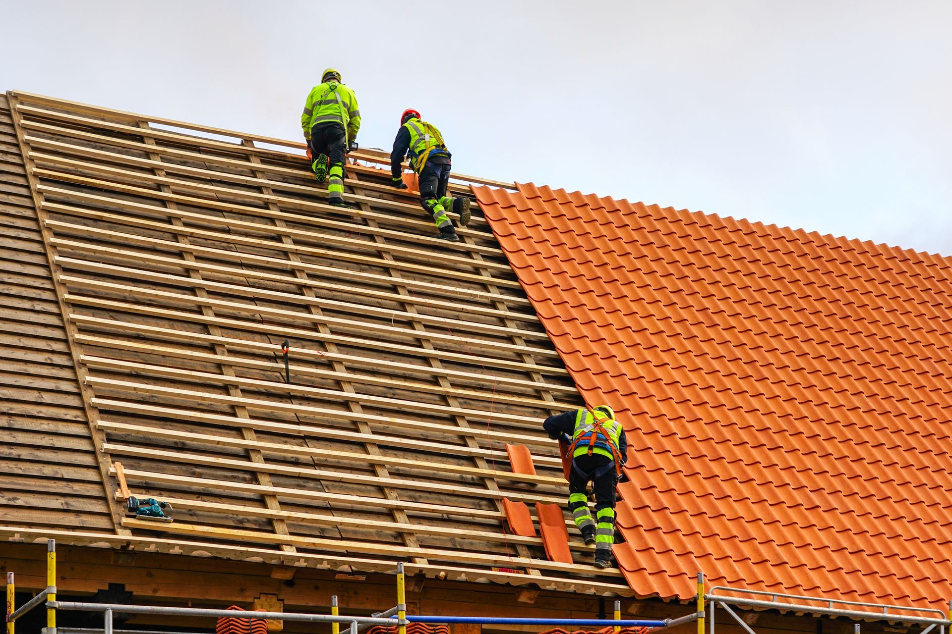 Roofers in green working on a house roof, replacing the tiles.