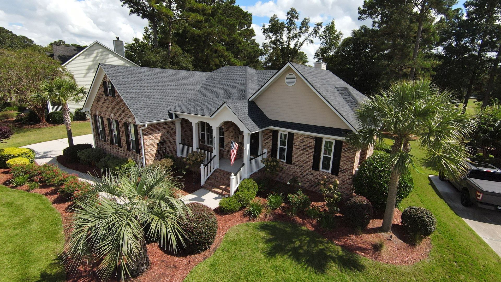 House with dark roof, brick and tan siding, surrounded by landscaping, green lawn, and trees.