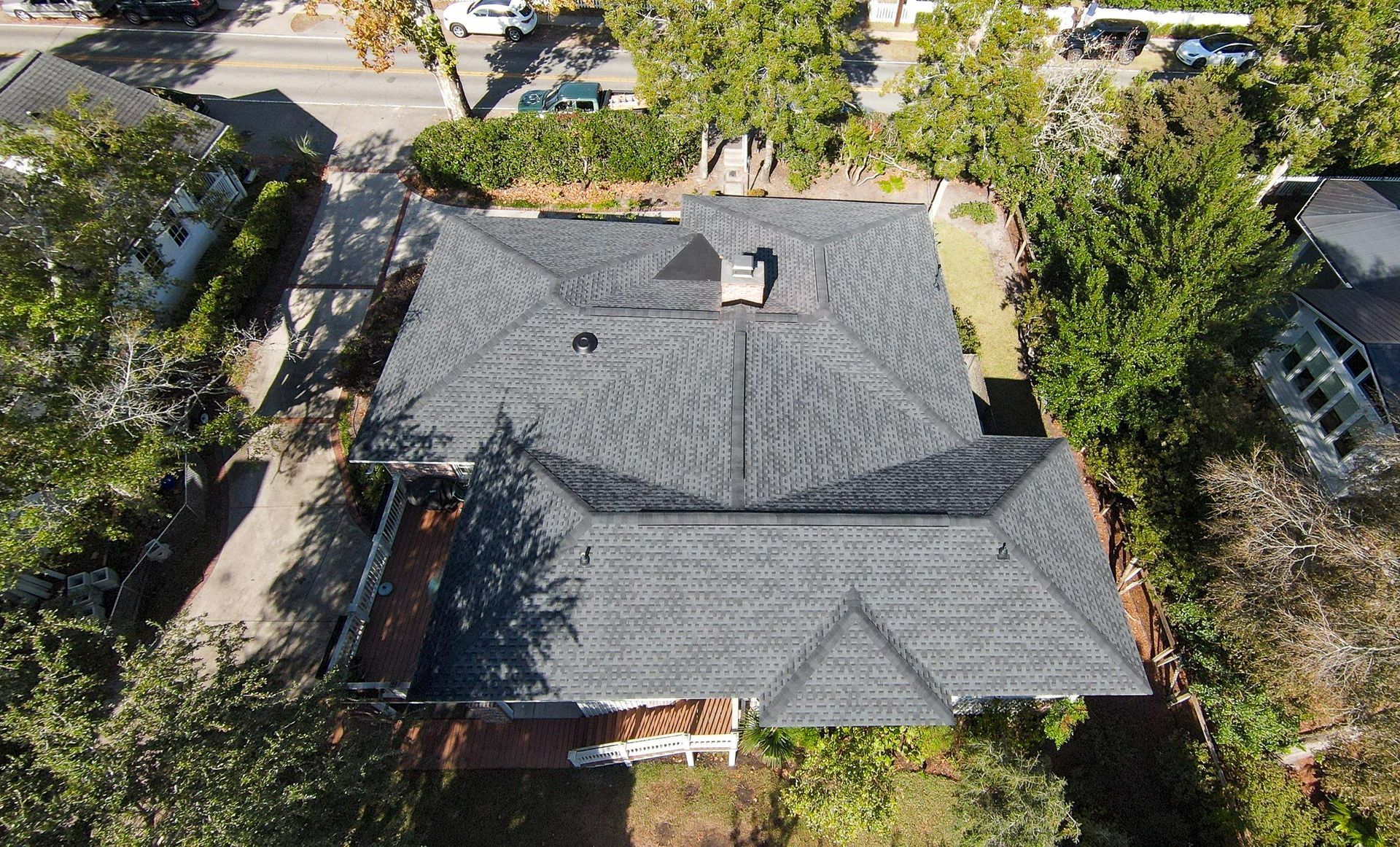 Overhead view of a house with a gray shingled roof, chimney, and surrounding greenery.