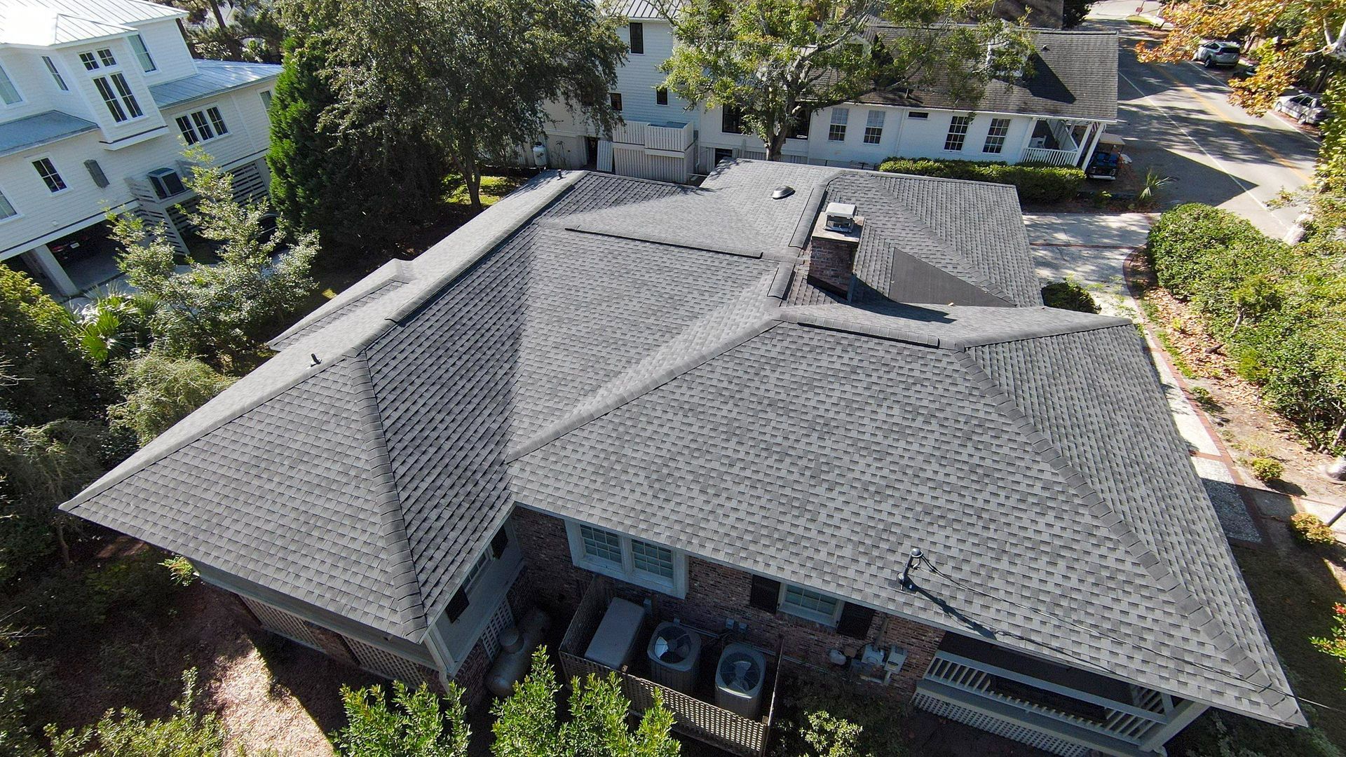 Overhead view of a house with a gray shingle roof, surrounded by trees and other buildings.