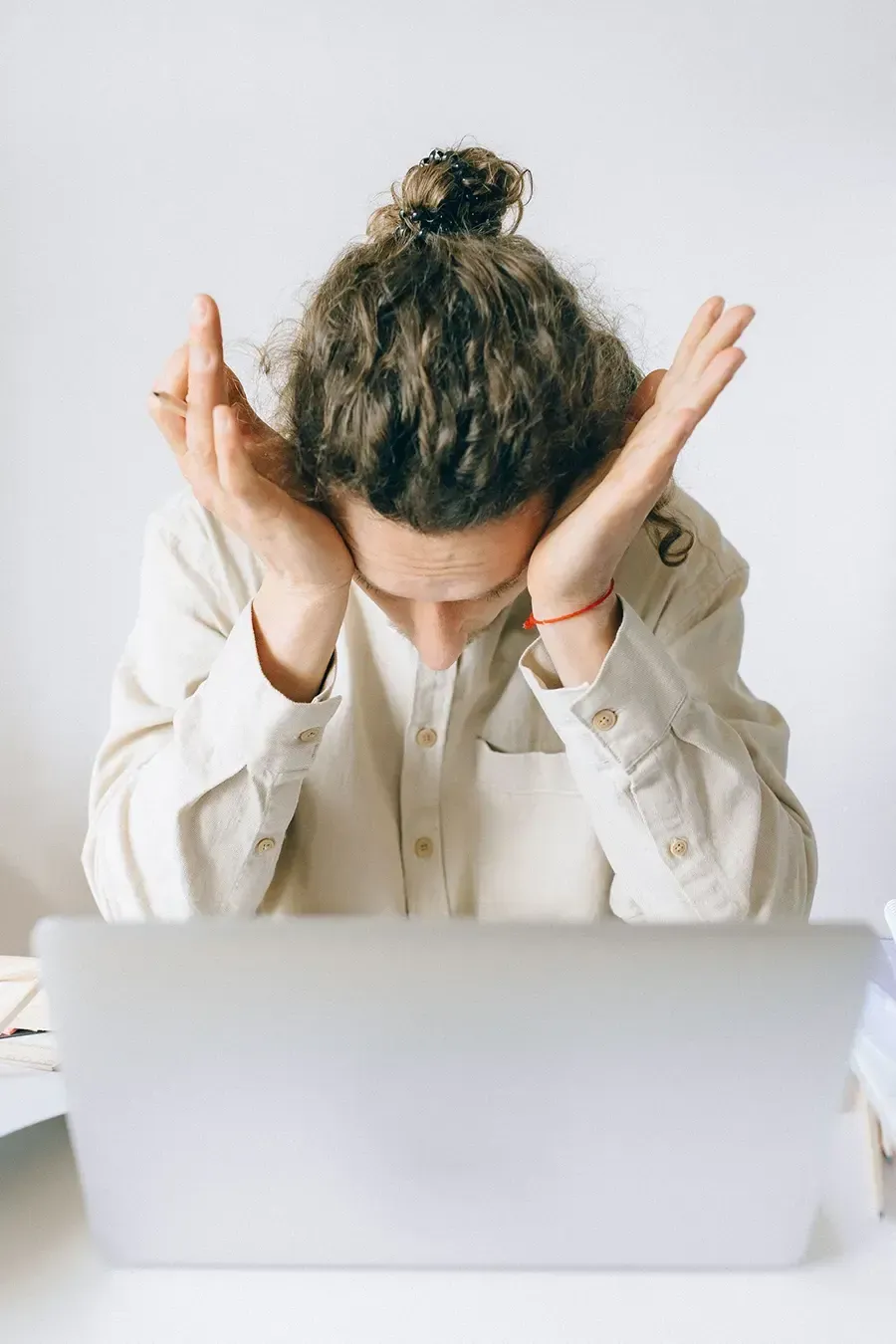 Person with head in hands behind laptop, appearing stressed or overwhelmed