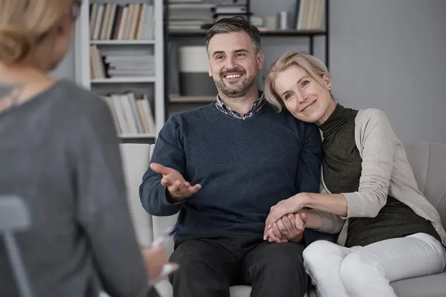 Two people sitting on a couch, smiling and holding hands in a bright office setting