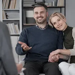 Two people sitting on a couch, smiling and talking with an unseen person in an office-like room