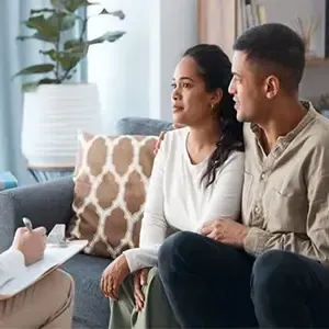 Two people listening to a therapist in a bright living room, seated on a couch.