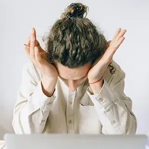 Person sitting at a desk with head in hands, appearing stressed or overwhelmed