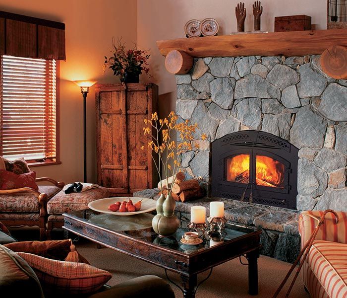 Cozy living room with stone fireplace, lit fire, wood mantel, and rustic coffee table by a window