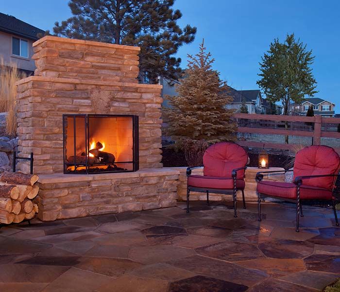 Stone outdoor fireplace beside two red chairs on a patio at dusk