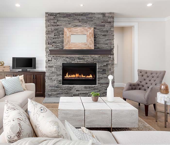 Cozy living room with stone fireplace, tufted chair, white sofa, and neutral decor