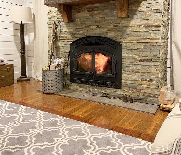 Living room fireplace with burning fire, stone surround, wood floor, and patterned rug