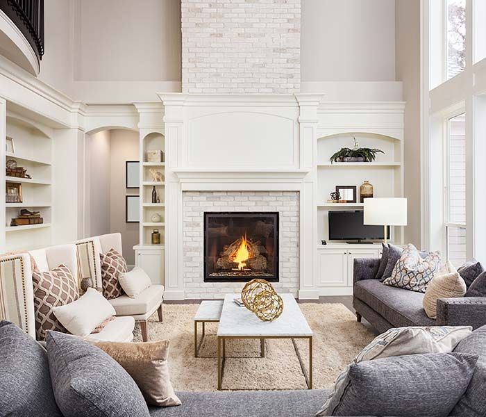 Bright living room with a lit fireplace, white walls, gray sofas, and a coffee table