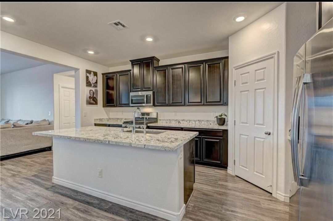 Modern kitchen with granite island, dark cabinets, stainless appliances, and wood flooring