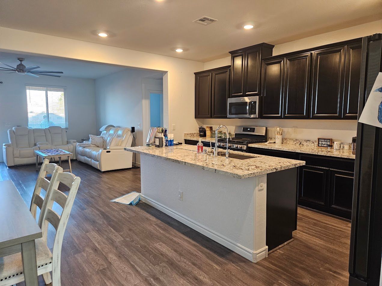 Open-concept kitchen and living room with dark cabinets, granite island, and light sectional sofa