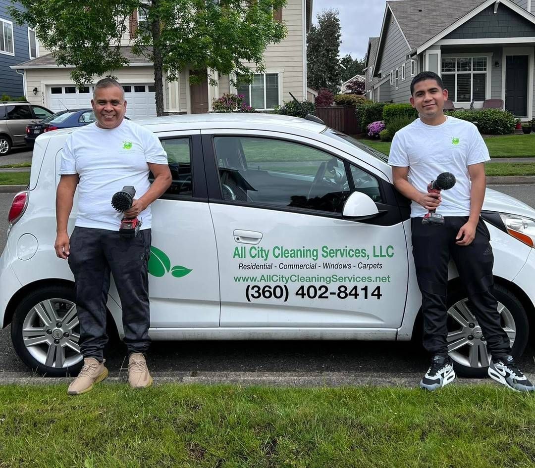 Two workers stand beside a white cleaning service van in a driveway.