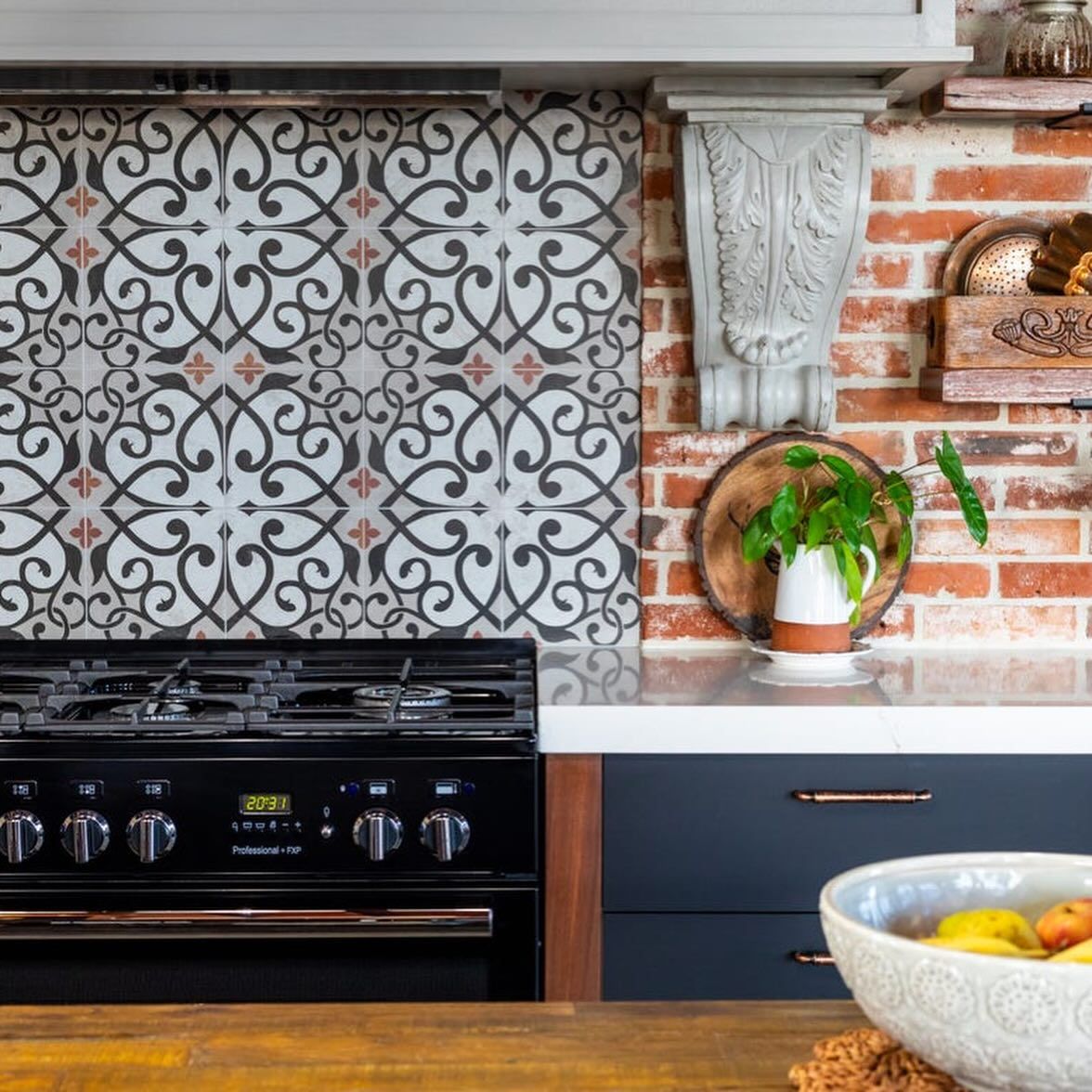 Kitchen with ornate tile backsplash, brick wall, black range, and blue cabinets — Cooloola Tile Company in Gympie, QLD