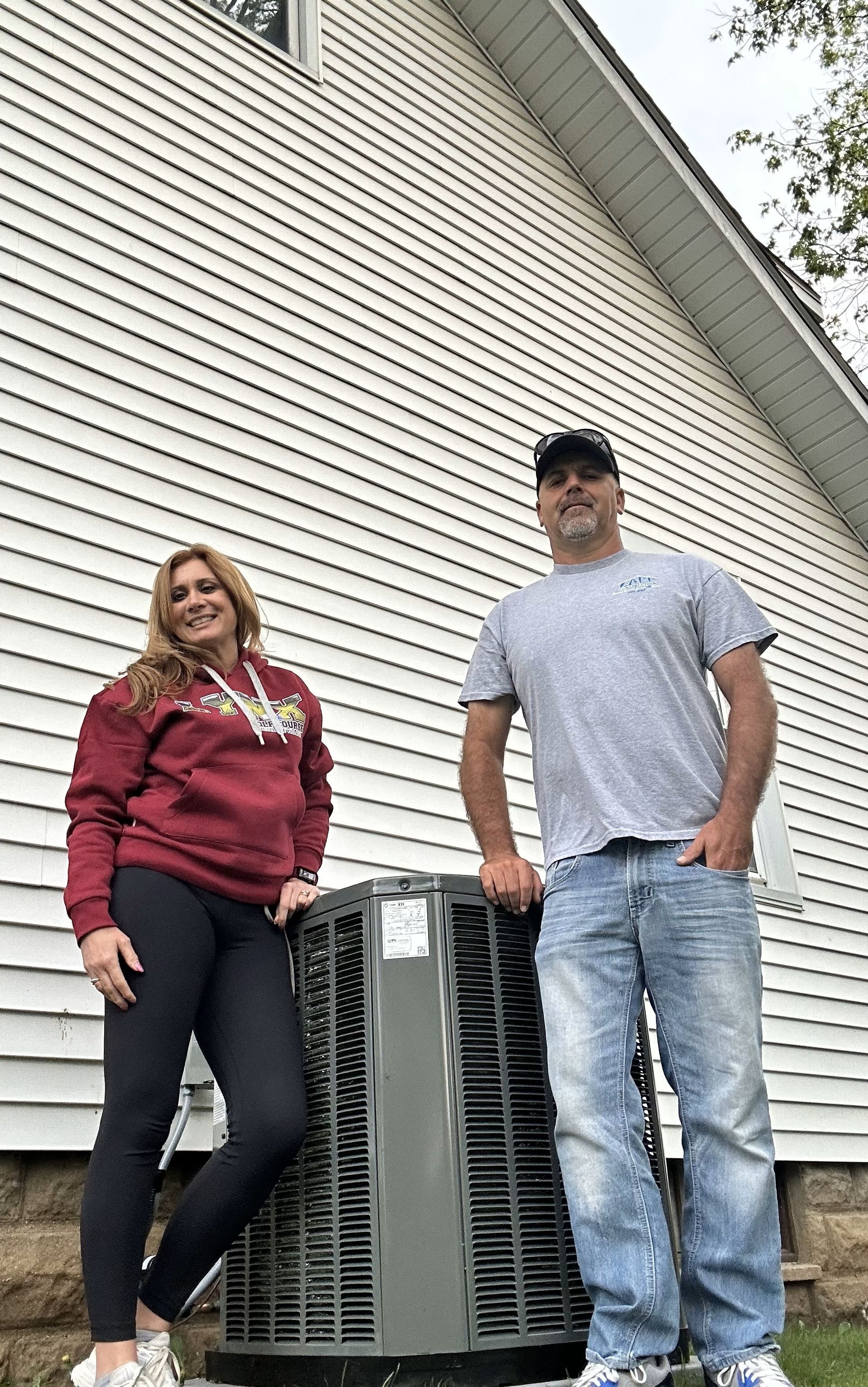 A man and a woman are standing next to an air conditioner outside of a house.