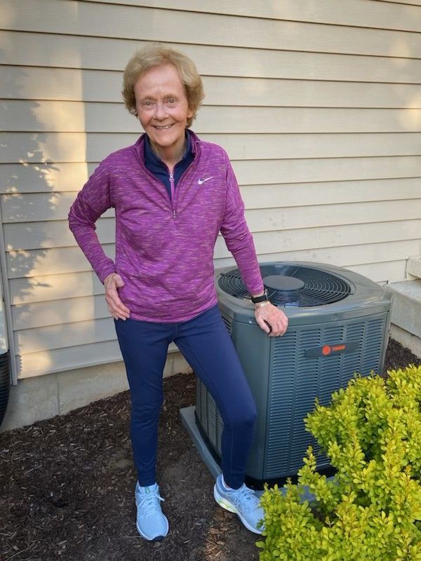 A woman in a purple shirt is standing next to an air conditioner.